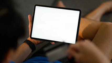 Closeup shot of casual man lying on couch and using digital tablet. White empty screen for advertise text