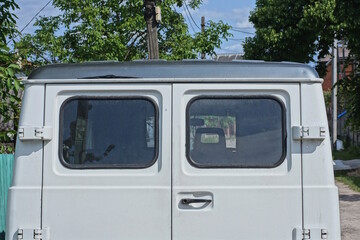 back of an old minibus with two windows on a white door on the street