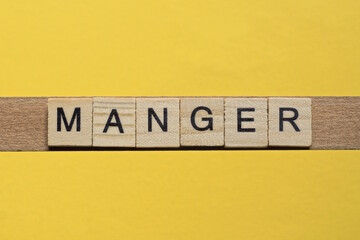 the word manger of gray small wooden letters lies on a yellow table