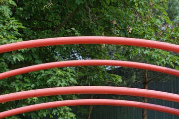 part of the construction of a row of red metal curved pipes on the street on the playground against...
