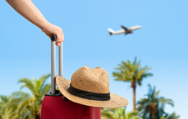 Woman with red suitcase standing on passengers ladder of airplane opposite sea with palm trees....