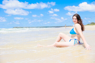 Fototapeta na wymiar ビーチに座るセクシーな水着姿の白人の女の子