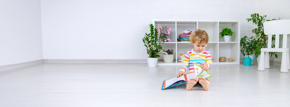 The child is looking at a book in the room. Selective focus.