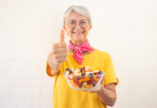 Smiling Senior Woman Holding Bowl Of Fresh Seasonal Fruit Ready To Eat Looking At Camera With Thumb Up. Breakfast Or Lunch, Eat Healthy And Dietary