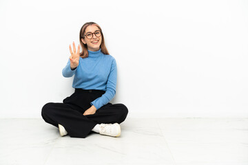 Young Caucasian woman sitting on the floor happy and counting three with fingers