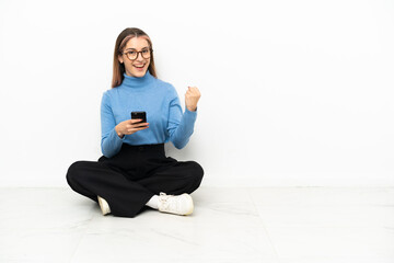 Young Caucasian woman sitting on the floor with phone in victory position