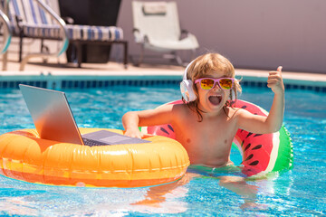 Summer travel and business concept. Kid working on laptop computer at poolside swimming pool. Summer online technology. Traveler relaxing on tropical sea in summer holidays.