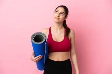 Young sport caucasian woman going to yoga classes while holding a mat and looking up