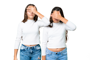 Friends girls holding gift and a birthday cake over isolated chroma key background covering eyes by hands. Do not want to see something
