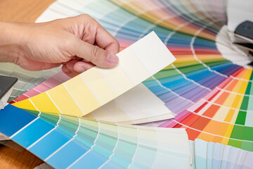 Designer hand choosing color swatch samples catalog or rainbow colour palette guide for selection...