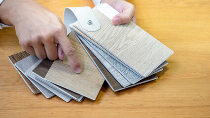 Designer hand choosing and pointing at wood texture laminate material samples or wooden palette catalog guide for interior architecture and furniture design work.
