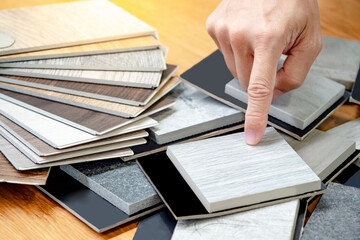 Architect hand choosing and pointing at stone material samples or tile texture collection on the table in studio. Designer working for interior architecture and furniture design project