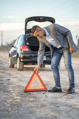 Young Latino man placing a warning triangle behind a broken down car.
