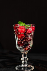 summer cocktail with cherry berries and mint sprigs in a transparent glass on a black background. bubbles in a glass. soft drink