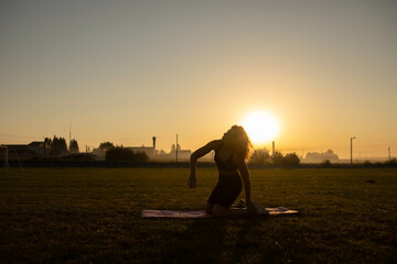 woman goes in for sports gymnastics yoga at dawn on the grass, a gymnastic mat for sports.