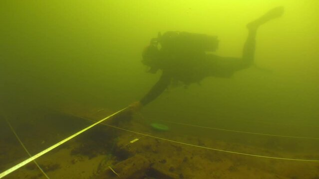 Underwater archaeological research: a scientist diver makes a plan of an 18th century wooden ship lying at the bottom of a river.