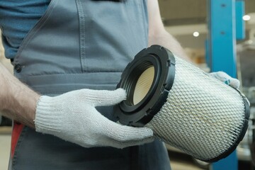 A mechanic holds an air filter for a car engine. Close-up. Checking the integrity and compliance of...