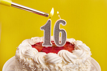 A candle in the form of the number 16, stuck in a festive cake, is lit. Celebrating a birthday or a...