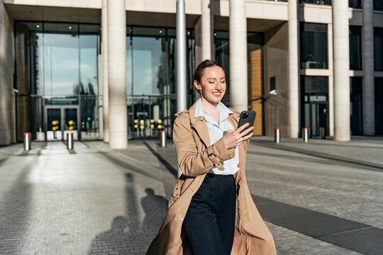 A woman using a phone writes SMS goes to work in the office, in formal street modern clothes.  The leader is a confident and happy and mentally healthy person.