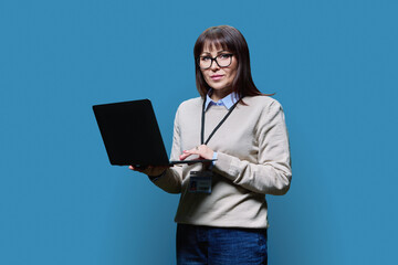 Middle aged confident serious female teacher using laptop on blue background