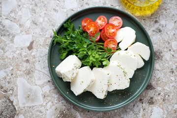 Sliced halloumi cheese with red cherry tomatoes and fresh parsley on a green plate, horizontal shot on a brown granite background, high angle view