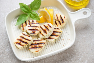 Beige serving tray with slices of grilled haloumi cheese, horizontal shot on a beige stone...