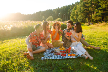 Attractive cheerful people gathering meeting eating watermelon embracing free time on the picnic  outdoors. People, lifestyle, travel, nature and vacations concept.