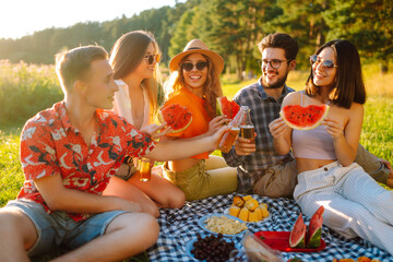 Attractive cheerful people gathering meeting eating watermelon embracing free time on the picnic  outdoors. People, lifestyle, travel, nature and vacations concept.