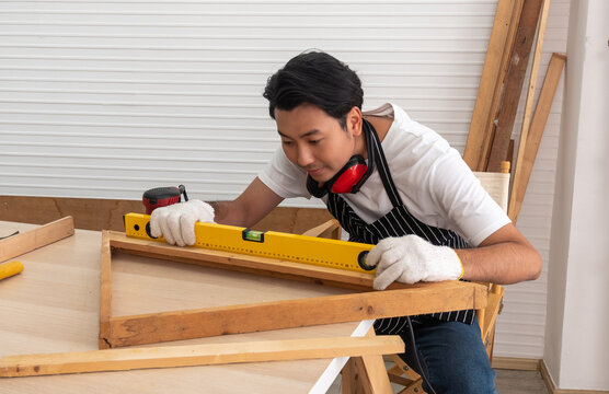 Asian carpenter in woodworking shop using inclinometer or spirit level to check wood slope. Own business, Small Business.