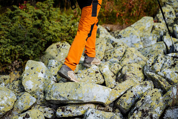 Shoes for traveling in the mountains, feet walking on stones in boots, trekking boots, sports shoes, stepping on stones, orange pants.