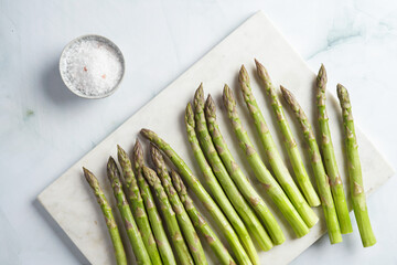 a bunch of fresh green raw asparagus on a marble board on a light pastel blue background, top view,...
