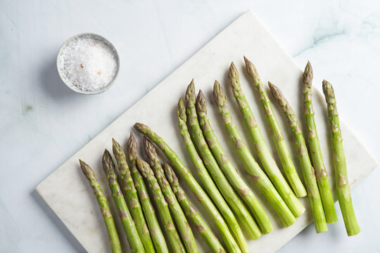 a bunch of fresh green raw asparagus on a marble board on a light pastel blue background, top view, flat lay
