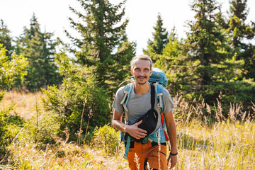 Fototapeta premium A guy cheerfully walks through the forest with a backpack, a tourist route, trekking alone, hiking in the forest, trekking equipment.