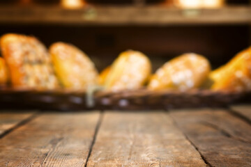 Old vintage wooden table with blurred rack with fresh bread in a bakery interior