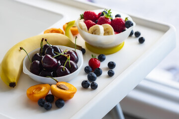Set of fresh fruits in children's plates stands on a highchair. Healthy food concept, seasonal summer vitamin food
