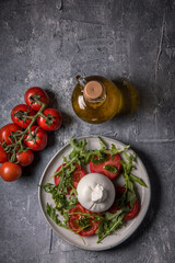 Burrata cheese with tomatoes, arugula and pesto sauce on a marble table.