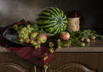 Still life with watermelon, grapes, apples and walnuts on a wooden table in dutch style. Close up