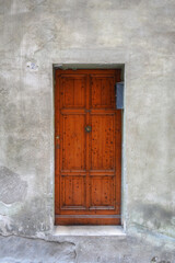 A frontal photo of A vivid wooden door inside a gray plaster door in Italy 
