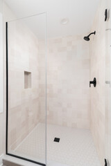 A shower with brown square tiles, black showerhead, and a hexagon tile floor.