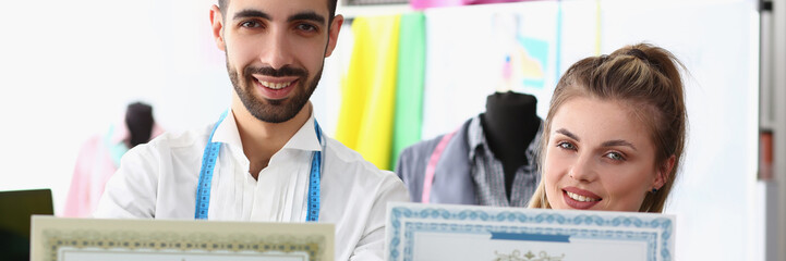 Man stylist and woman seamstress hold certificate of quality for clothes. Atelier tailoring...