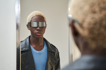 Dark skinned blonde man wearing trendy sunglasses looking at the mirror