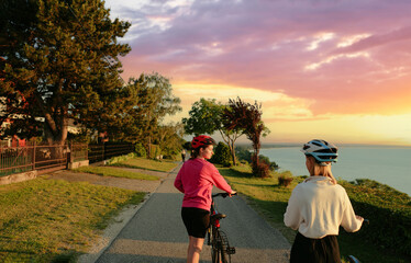 Two women walking on the sea promenade with bicycle. Back view.