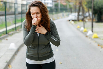 Young sporty woman coughing while walking on the street