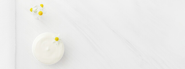 White nourishing cream with chamomile in a white jar.