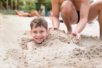 Two brothers having fun on beach in summer after swimming, the older brother burying the younger...