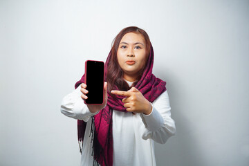 Shocked Asian woman wearing hijab, showing copy space on her phone screen, isolated by white background