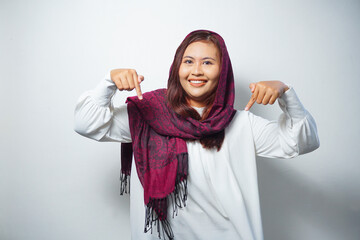 Asian Muslim woman wearing hijab pointing at the copy space below her, isolated by white background