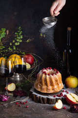 Woman's hand cooking homemade apple bundcake. Two glasses of red wine, bundcake, fruits on the dark brown table. Dark photography - 611674727