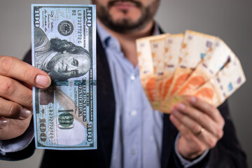 Hombre sosteniendo un billete de 100 dolares y billetes de pesos argentino, en concepto de...