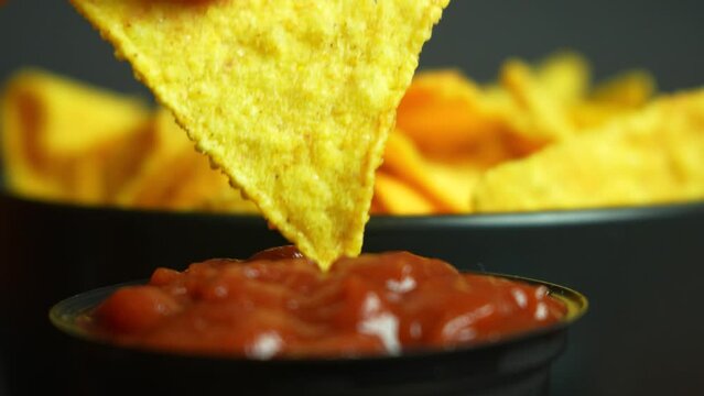 Extremely close up nacho chip dipping into tomato sauce